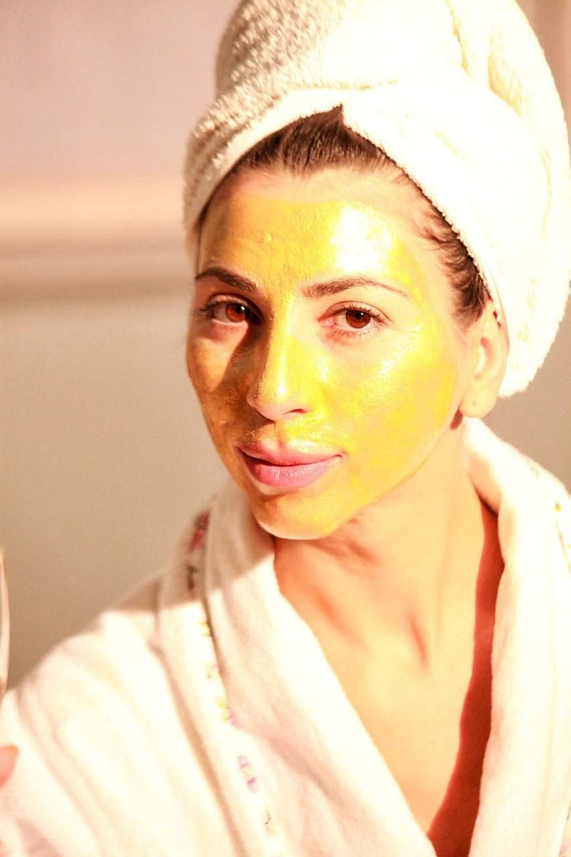 Woman with a radiant turmeric face mask from Radiant Revival Turmeric skincare kit in a white towel and robe